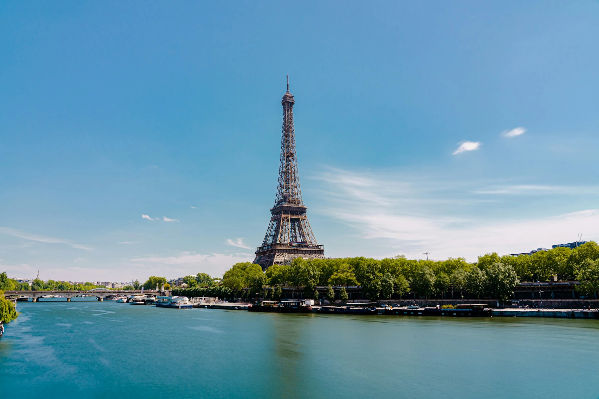 Summer sunshine on the Seine, with green riverbanks, boats and the Eiffel Tower.